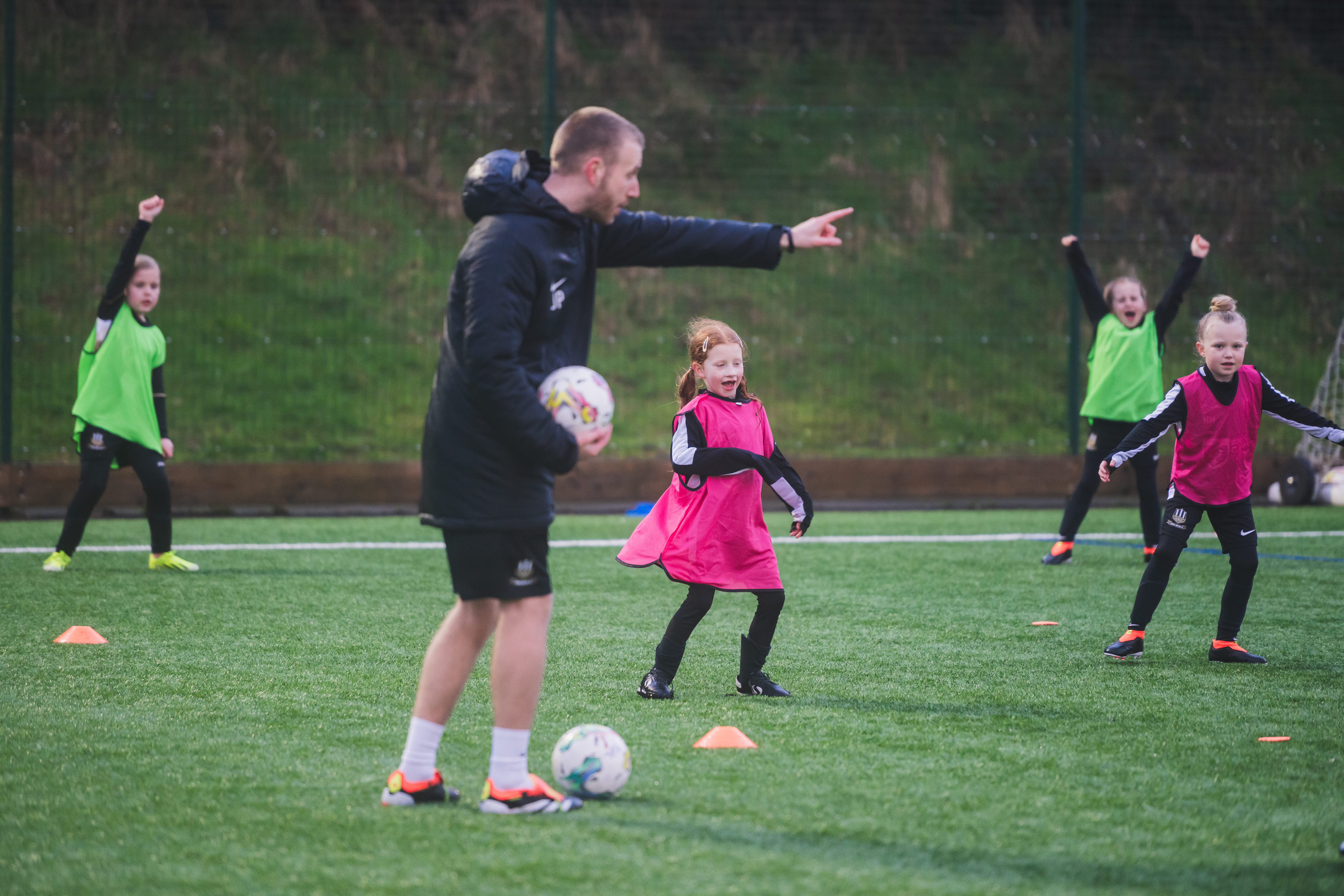 A coach with the girl team on a pitch holding a football